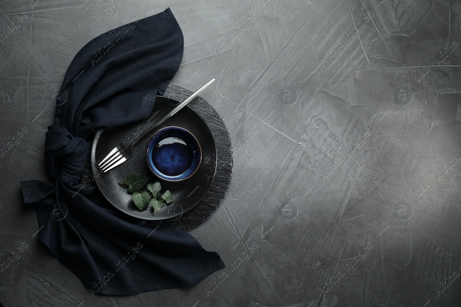 Photo of Stylish table setting. Dishes, fork, napkin and green leaves on grey surface, top view with space for text