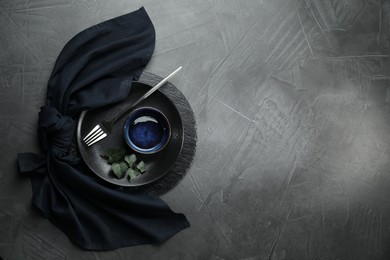 Stylish table setting. Dishes, fork, napkin and green leaves on grey surface, top view with space for text