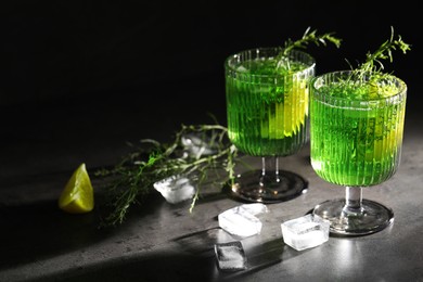 Photo of Glasses of homemade refreshing tarragon drink, ice cubes and sprigs on grey table. Space for text