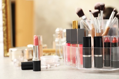 Photo of Lipstick holder with different makeup products on dressing table near mirror