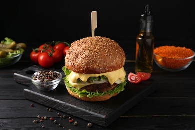 Tasty vegetarian burger and ingredients on black wooden table