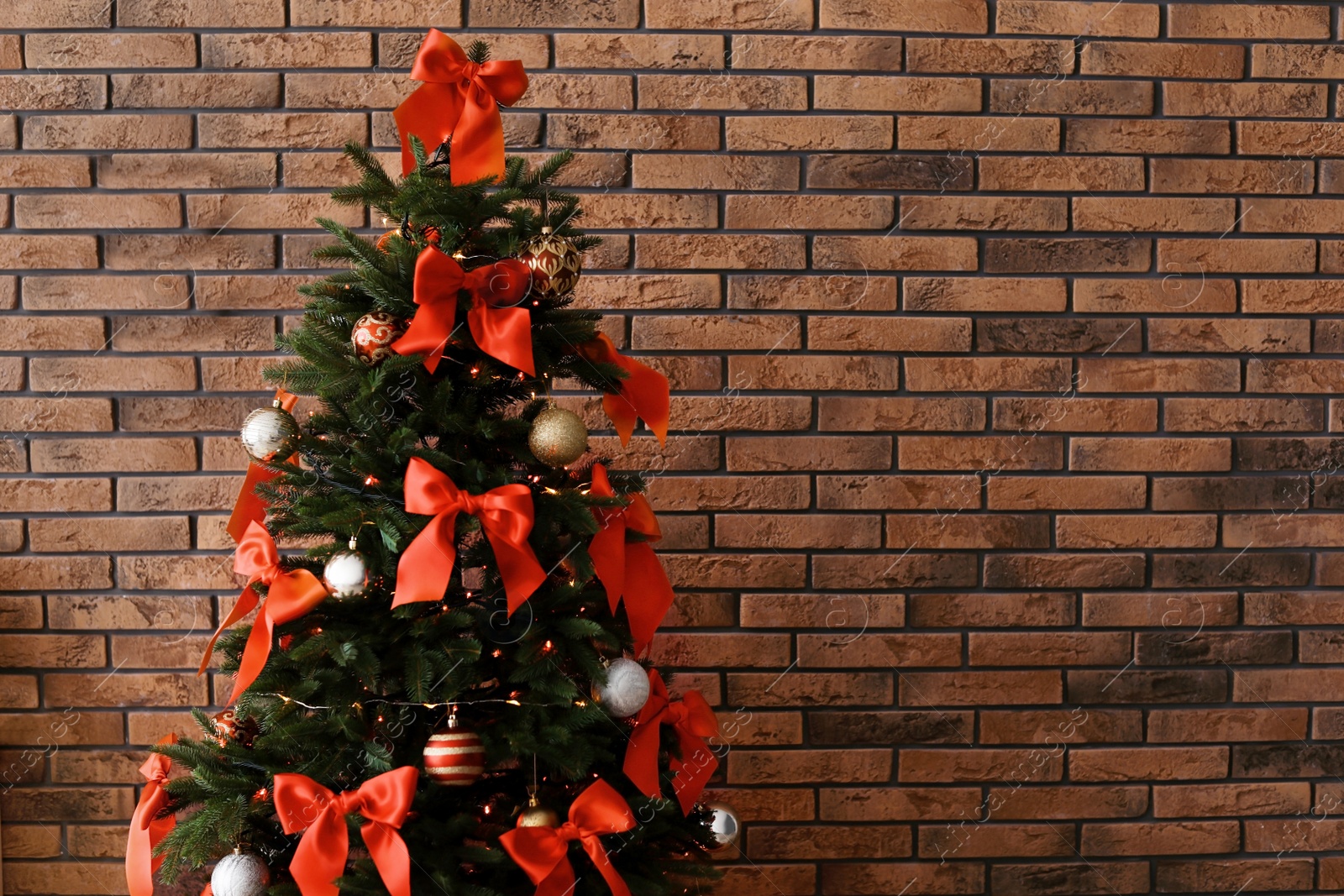 Photo of Christmas tree with stylish decor near brick wall