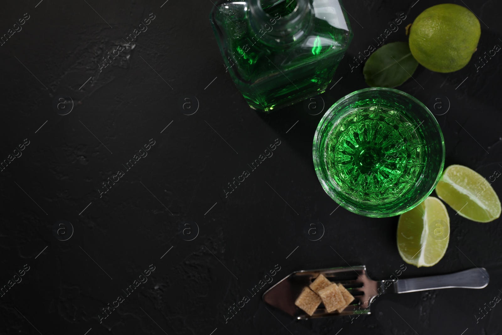 Photo of Absinthe, spoon, brown sugar and lime on black table, flat lay with space for text. Alcoholic drink