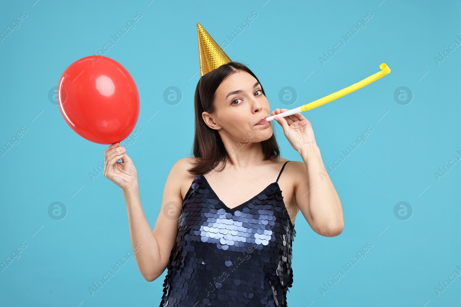 Photo of Young woman in party hat with blower on light blue background