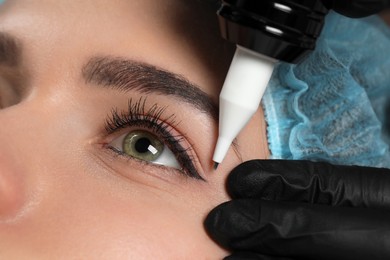 Photo of Young woman undergoing procedure of permanent eye makeup, closeup