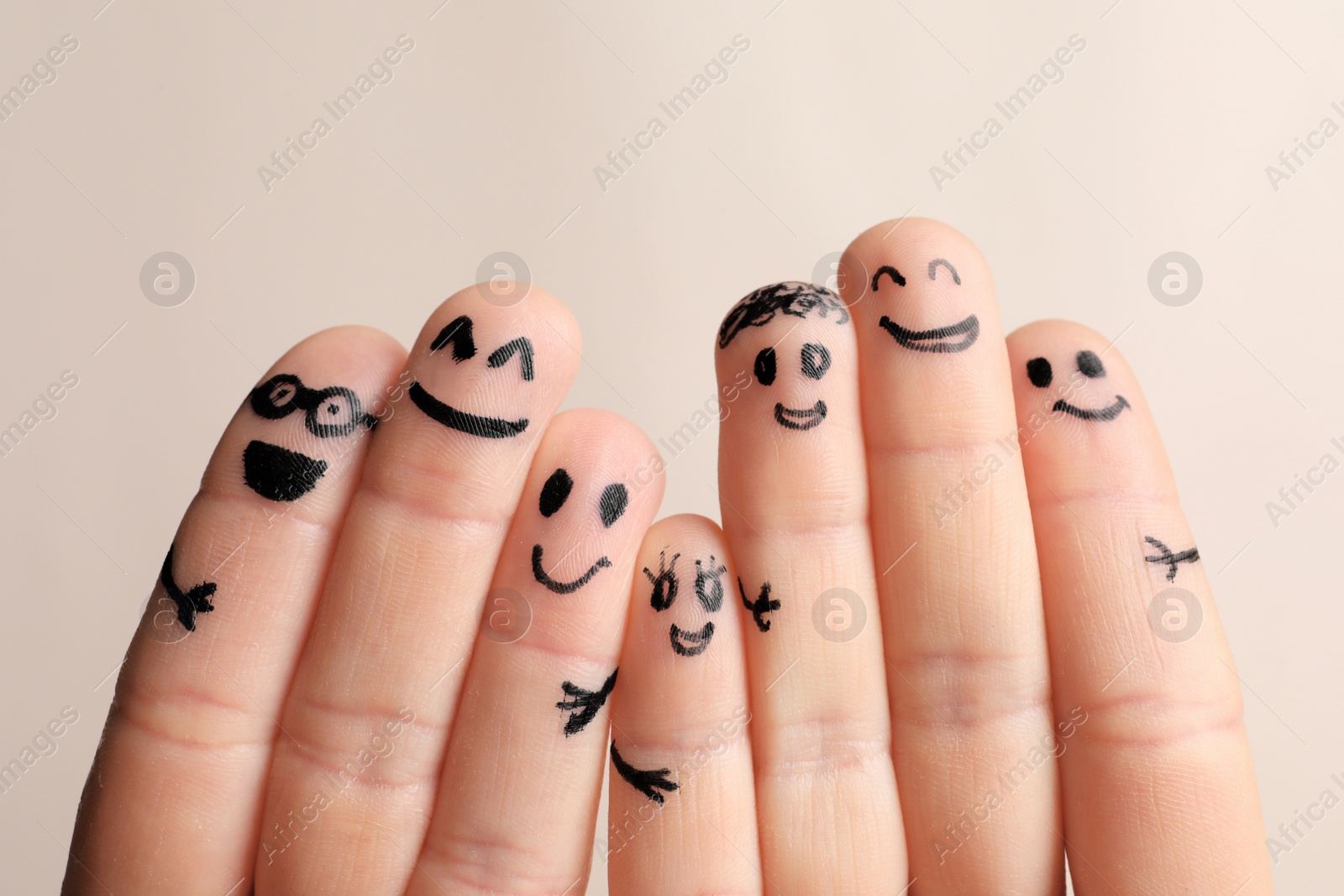 Photo of Fingers with drawings of happy faces against light background. Unity concept