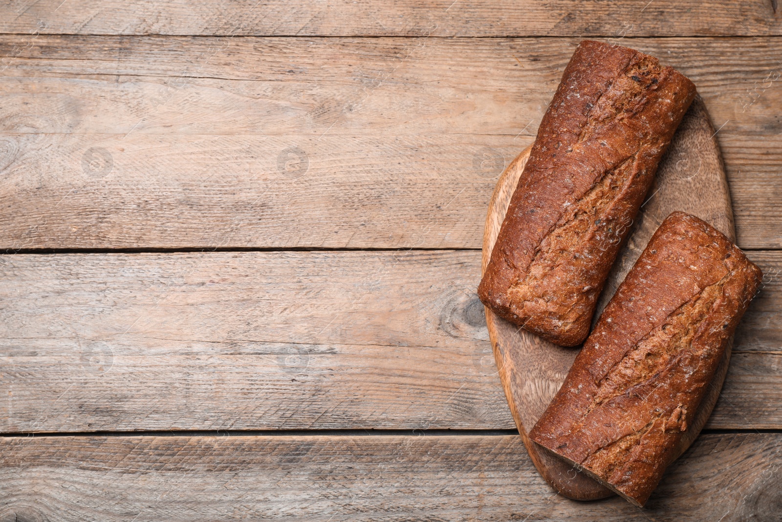 Photo of Cut rye baguette on wooden table, top view. Space for text