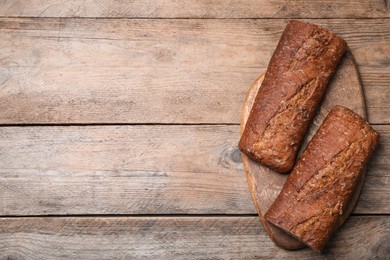 Photo of Cut rye baguette on wooden table, top view. Space for text