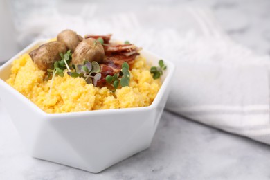 Photo of Cooked cornmeal with bacon, mushrooms and microgreens in bowl on white marble table, closeup. Space for text