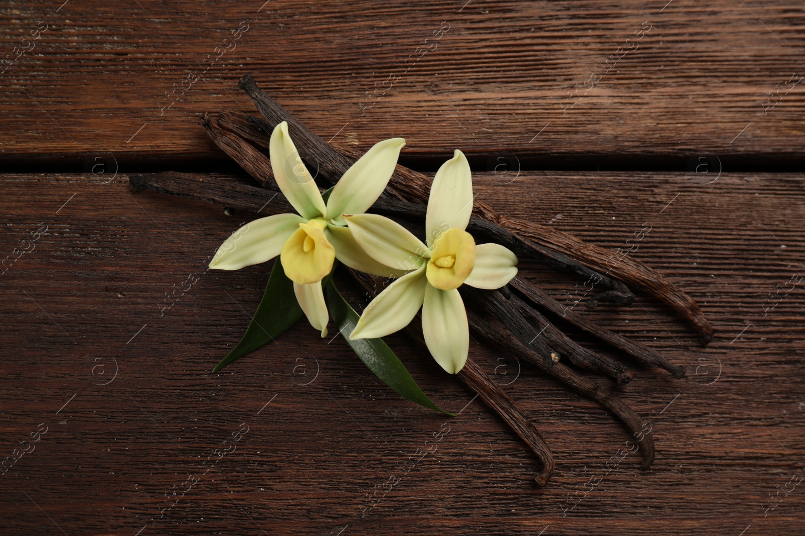 Photo of Beautiful vanilla flowers and sticks on wooden table, flat lay