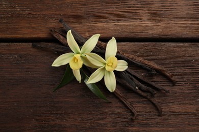 Beautiful vanilla flowers and sticks on wooden table, flat lay