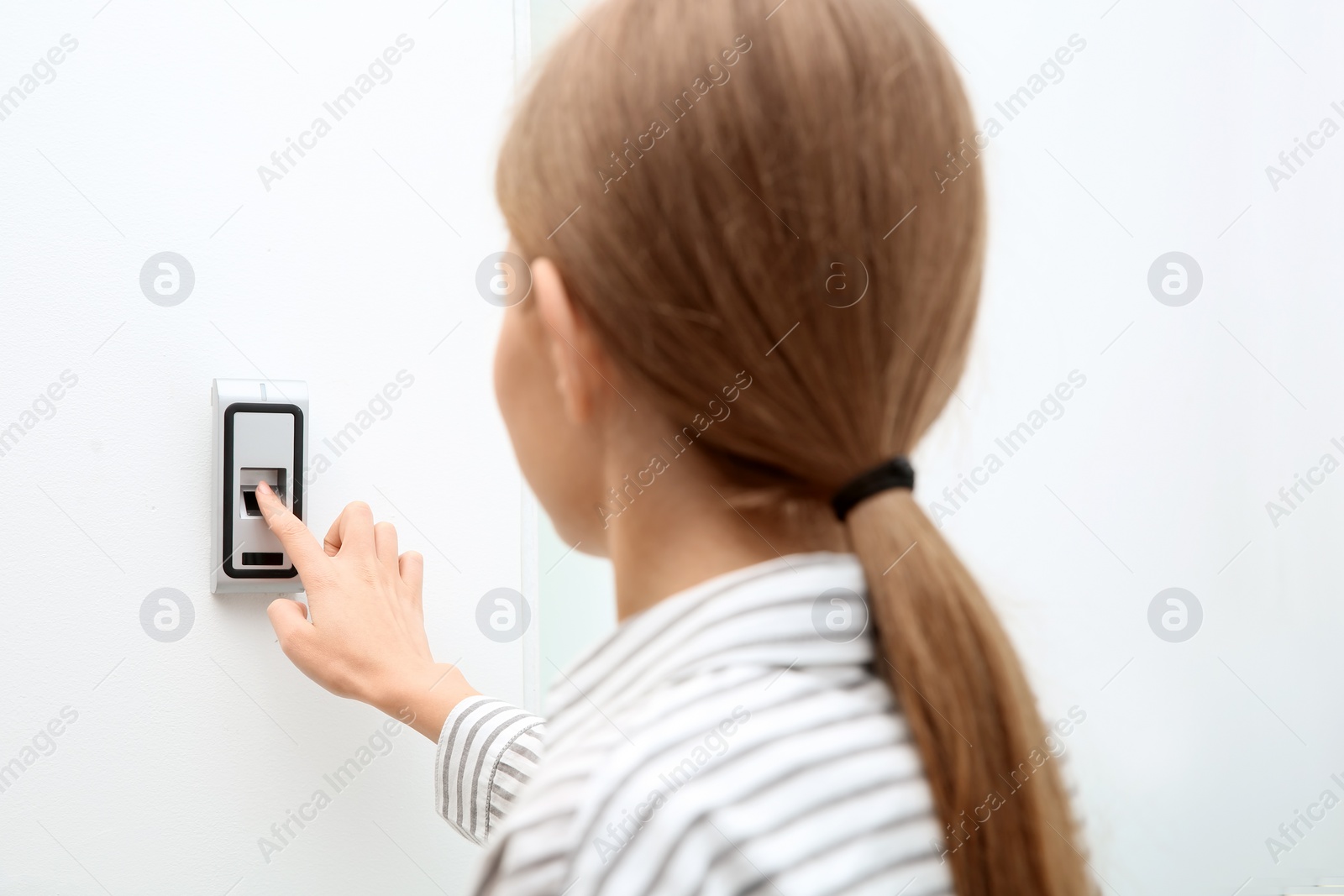 Photo of Young woman pressing fingerprint scanner on alarm system indoors