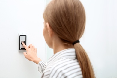 Photo of Young woman pressing fingerprint scanner on alarm system indoors