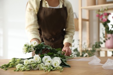 Florist making beautiful bouquet at table in workshop, closeup