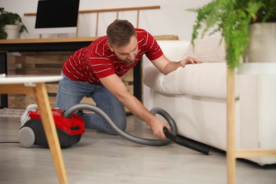 Young man using vacuum cleaner in living room