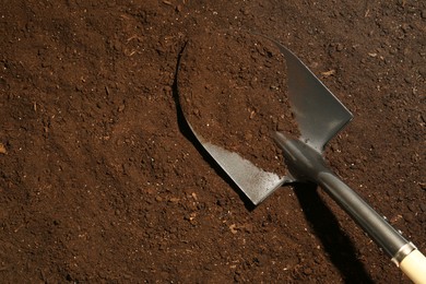 Photo of Metal shovel on fertile soil, top view and space for text. Gardening tool