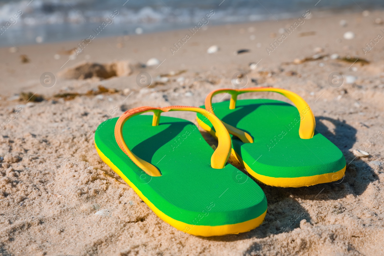 Photo of Stylish green flip flops on beach, closeup