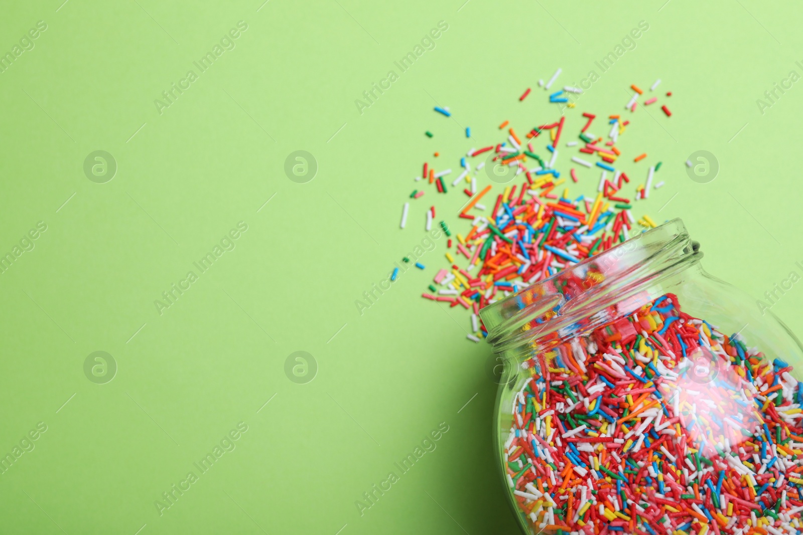 Photo of Colorful sprinkles and jar on green background, flat lay with space for text. Confectionery decor