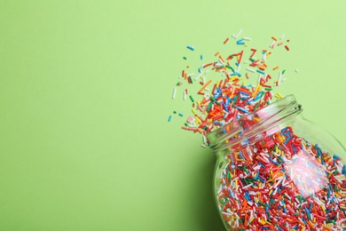 Colorful sprinkles and jar on green background, flat lay with space for text. Confectionery decor