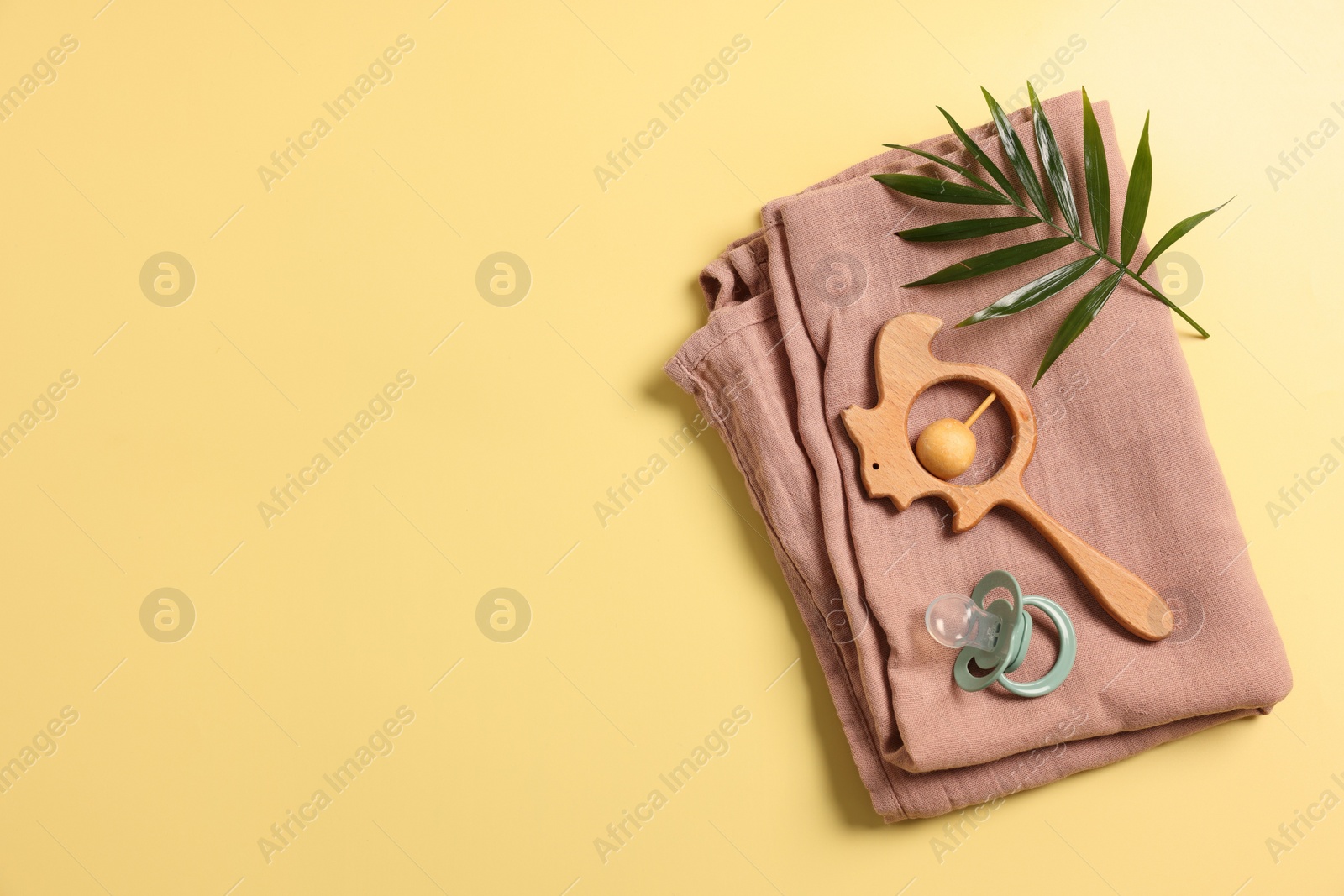 Photo of Baby accessories. Wooden rattle, pacifier, palm leaf and cloth on yellow background, top view. Space for text