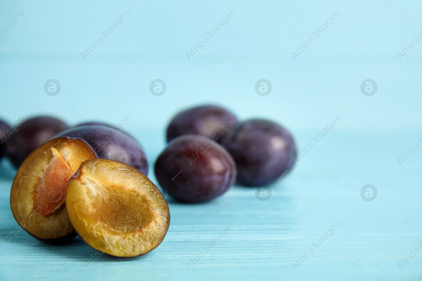 Photo of Delicious ripe plums on light blue wooden table, closeup. Space for text