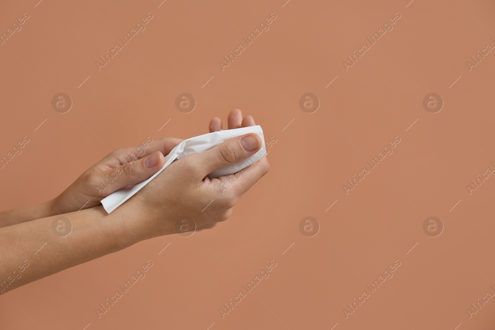 Photo of Woman cleaning hands with paper tissue on light brown background, closeup. Space for text