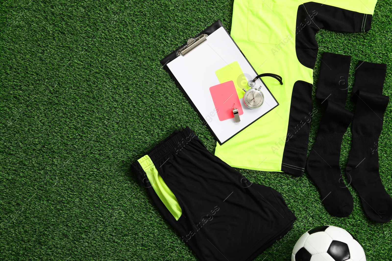 Photo of Uniform, soccer ball and other referee equipment on green grass, flat lay. Space for text