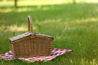 Photo of Wicker basket with blanket on green grass in park, space for text. Summer picnic