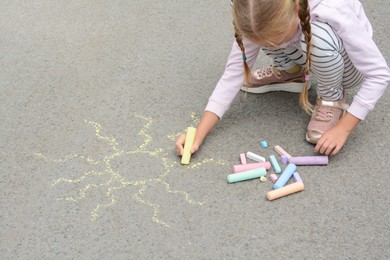 Photo of Little child drawing sun with chalk on asphalt