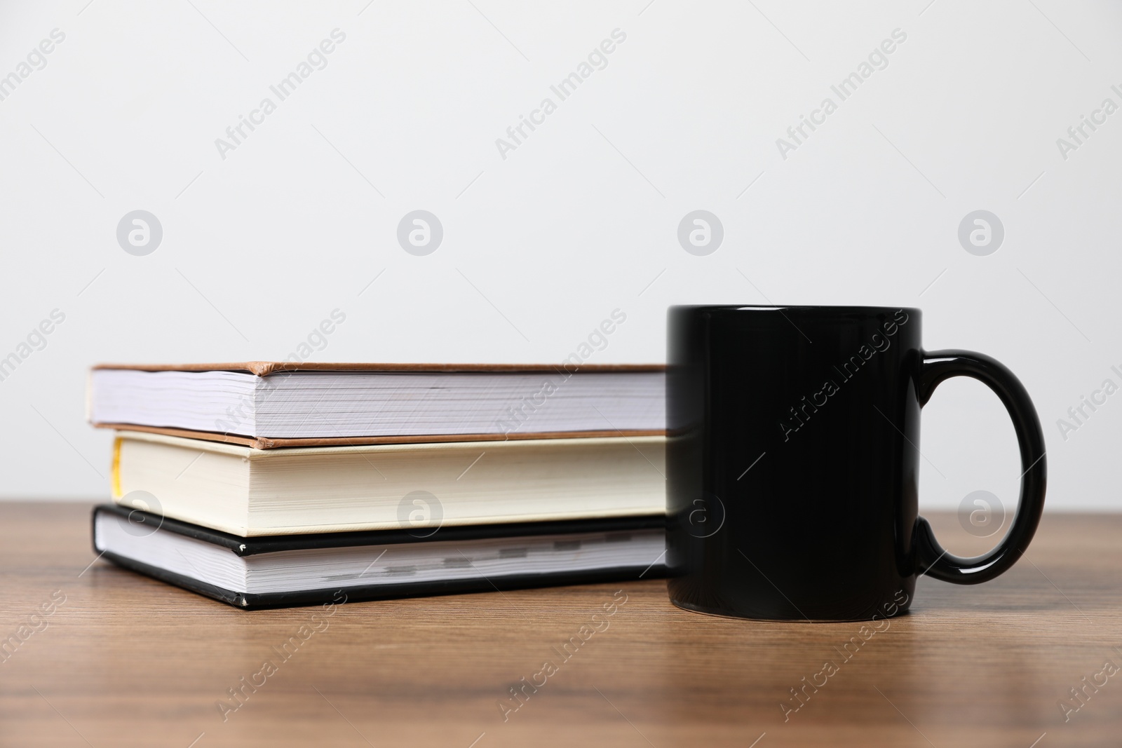 Black ceramic mug and stack of books on wooden table Photo of Black ceramic mug and stack of books on wooden table