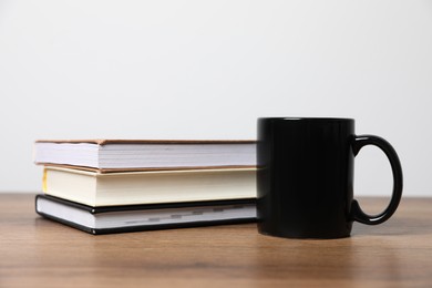 Photo of Black ceramic mug and stack of books on wooden table