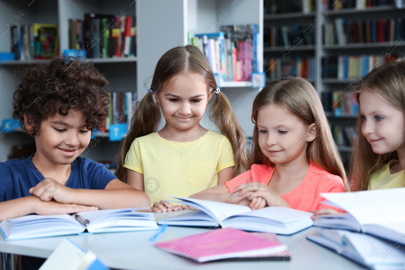 Photo of Group of happy little children reading books at table in library