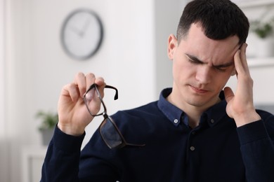 Photo of Young man with glasses suffering from headache in office