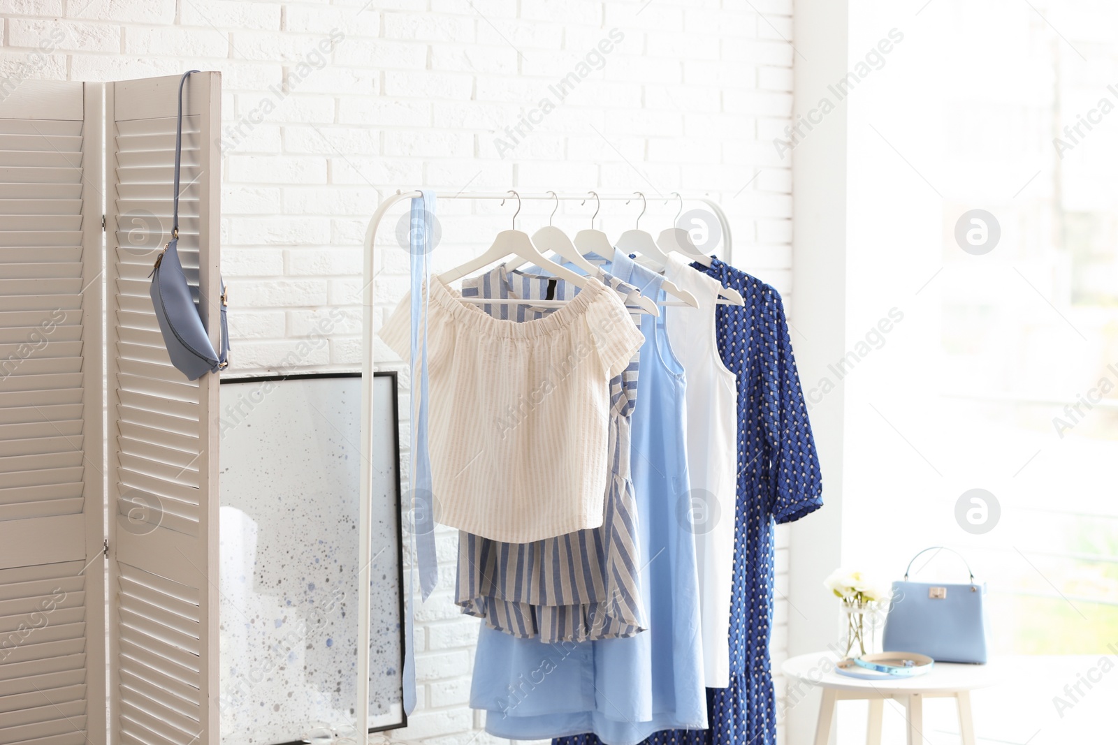 Photo of Wardrobe rack with women's clothes at white brick wall in room