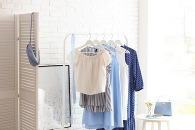 Photo of Wardrobe rack with women's clothes at white brick wall in room
