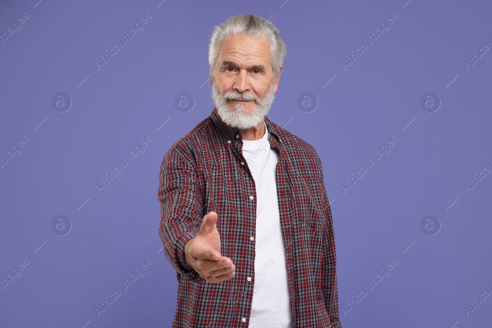 Photo of Senior man welcoming and offering handshake on purple background