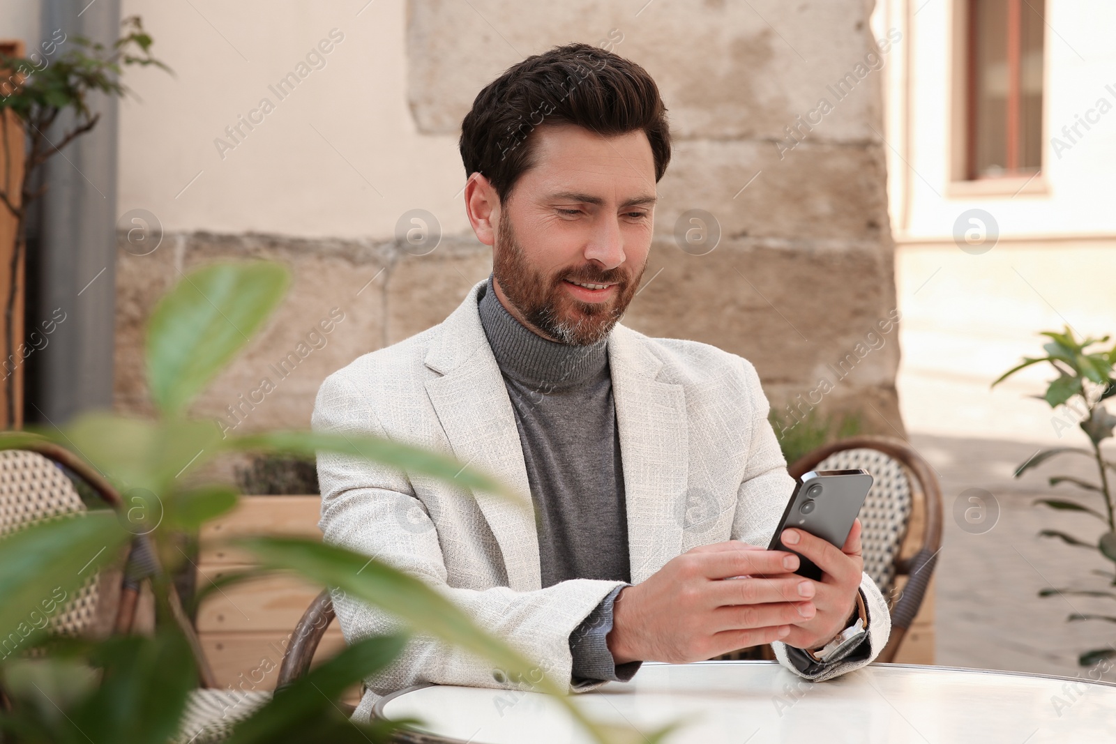 Photo of Handsome man sending message via smartphone at table outdoors