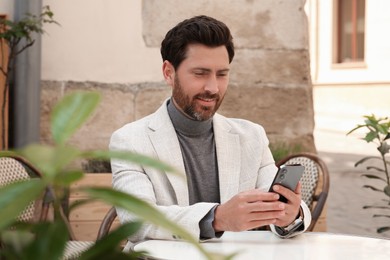 Handsome man sending message via smartphone at table outdoors