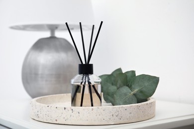 Photo of Reed diffuser with lamp and eucalyptus on white table, closeup