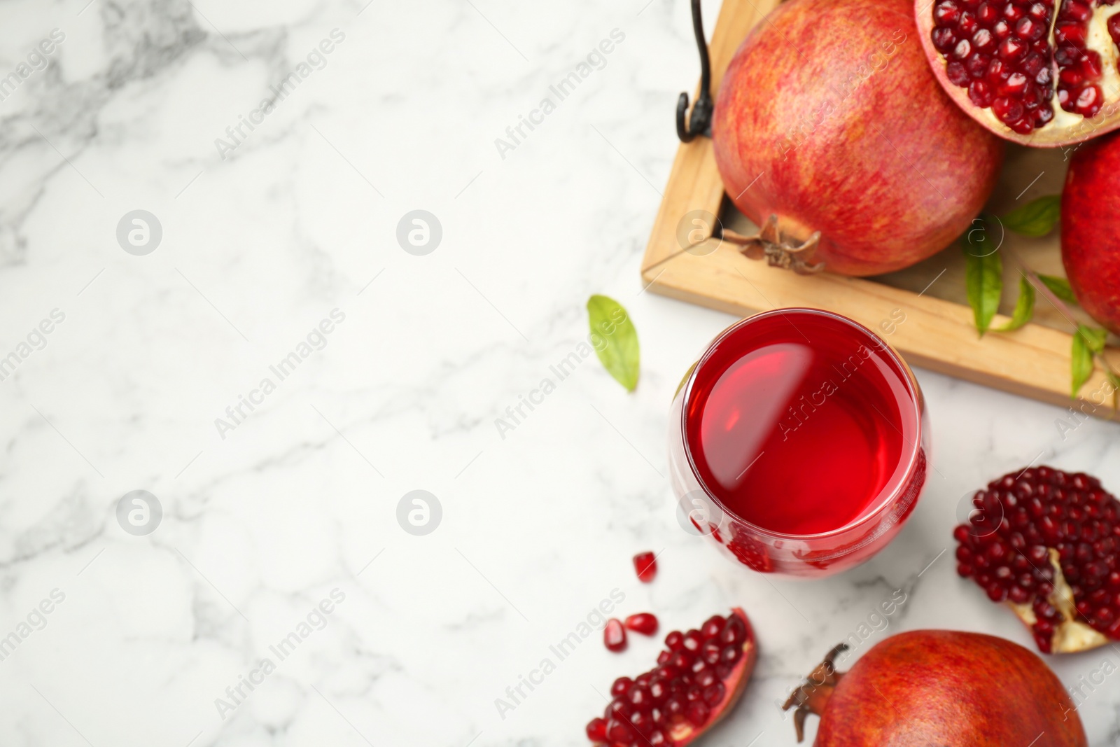 Photo of Tasty pomegranate juice in glass and fresh fruits on white marble table, flat lay. Space for text
