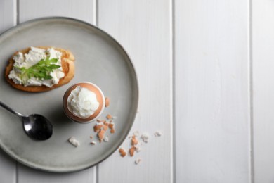 Fresh soft boiled egg in cup and sandwich on white wooden table, top view. Space for text