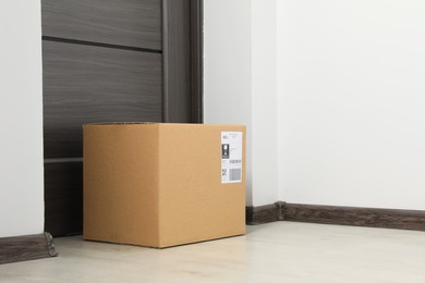 Photo of Cardboard box on floor near entrance. Parcel delivery service