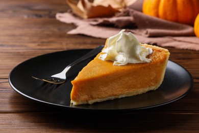 Photo of Piece of delicious pumpkin pie with whipped cream and fork on wooden table, closeup