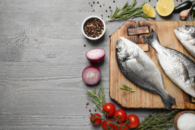 Flat lay composition with raw dorada fish on grey wooden table, space for text