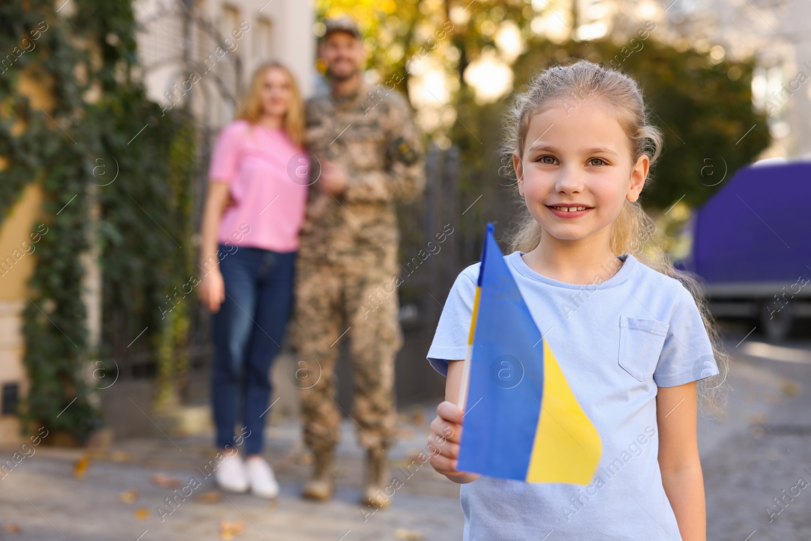 Photo of Child with Ukrainian flag, her father in military uniform and mother on city street, space for text. Family reunion