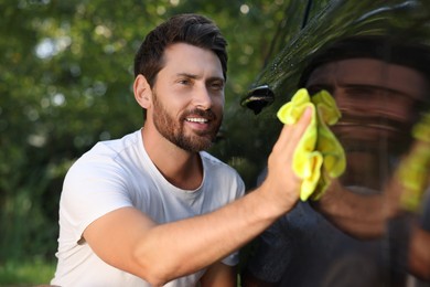 Photo of Happy man washing car door with rag outdoors