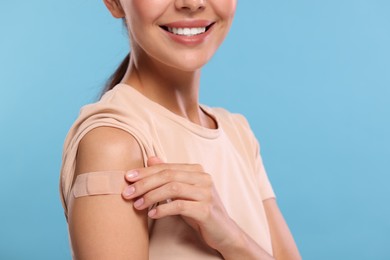Photo of Woman with sticking plaster on arm after vaccination against light blue background, closeup
