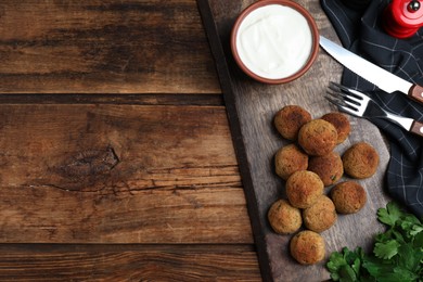 Delicious falafel balls with sauce on wooden table, flat lay. Space for text