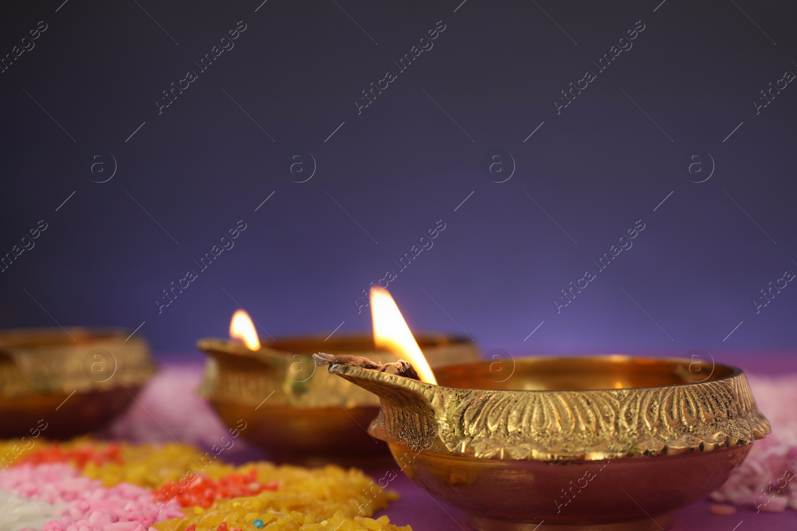 Photo of Diwali celebration. Diya lamps and colorful rangoli against purple background, closeup