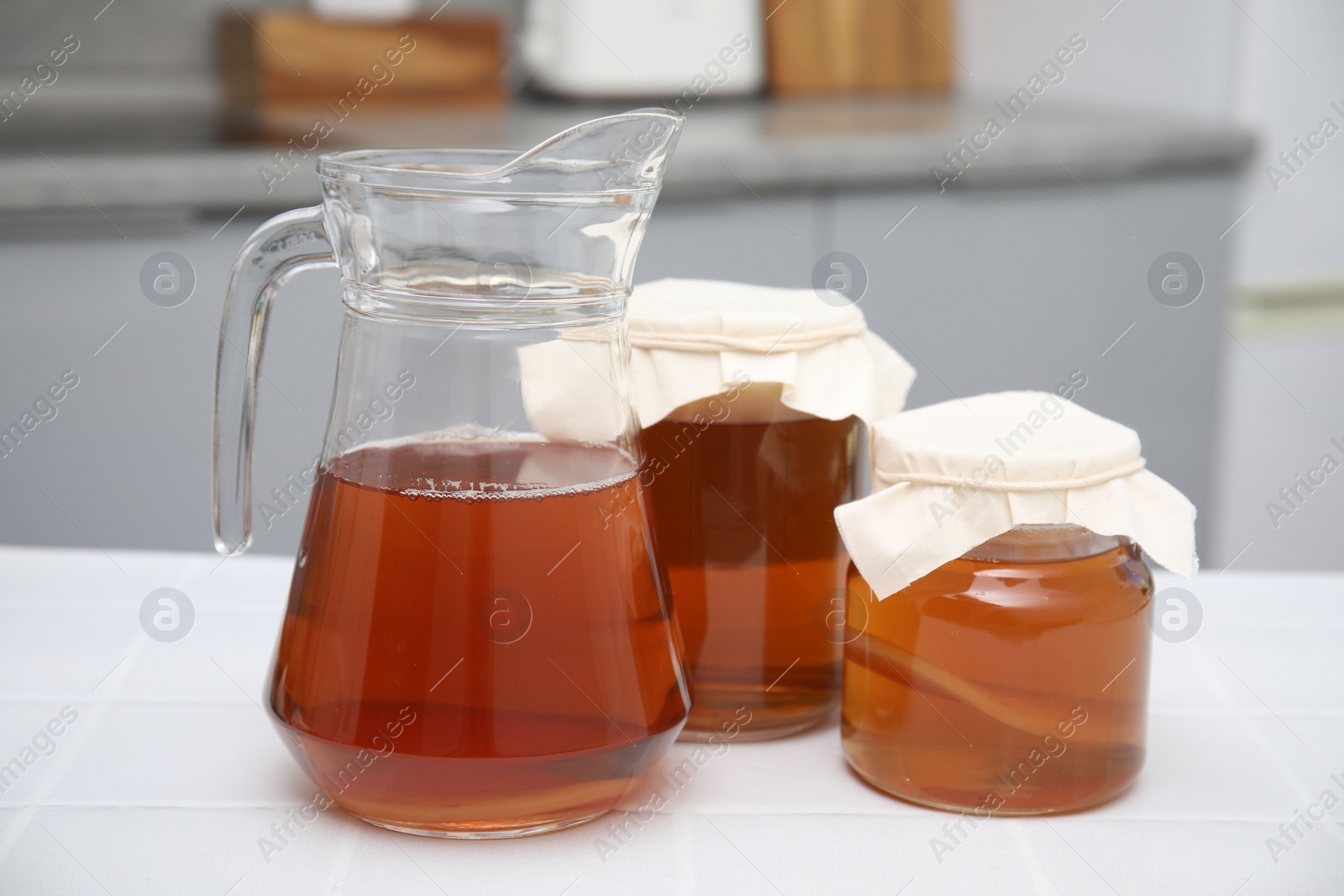 Photo of Homemade fermented kombucha in glass jars and jug on white table in kitchen